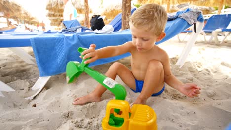 bambino seduto sulla sabbia gioca da solo con un raschietto di plastica, durante il giorno