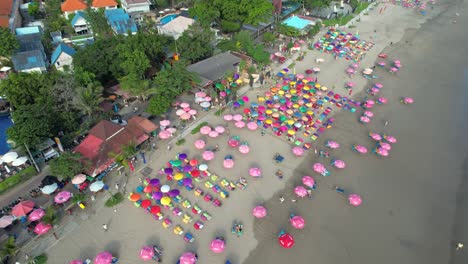 Playa-Doble-Seis-En-Bali---La-Gente-Disfruta-De-Un-Día-Soleado-En-La-Playa-De-Arena-Bajo-Sombrillas,-Vista-Aérea-De-Arriba-Hacia-Abajo