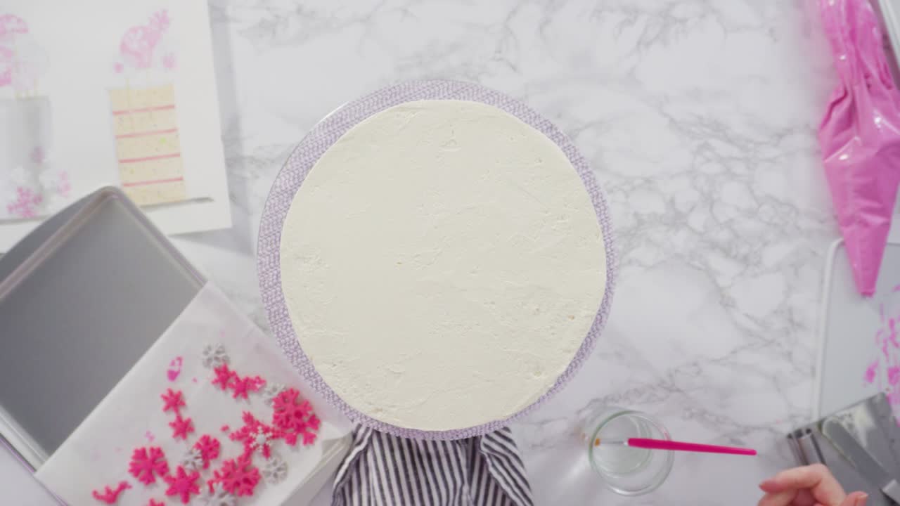 decorando el pastel funfetti redondo con copos de nieve de fondante rosado y blanco.
