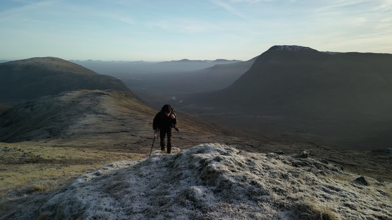 Glen Coe, Scottish Highlands - aerial over the mountains in winter with hill walker hiking forwards