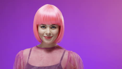 retrato de una mujer elegante con una peluca rosa sonriendo a la cámara y lanzando besos