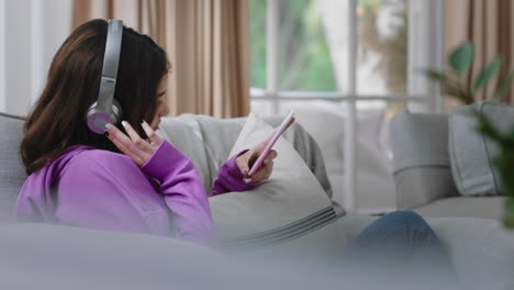 happy teenage girl listening to music wearing headphones relaxing on sofa at home texting with smartphone enjoying sharing lifestyle on social media