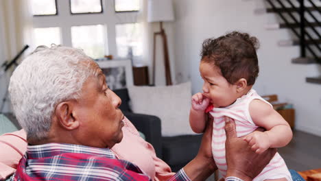grandparents sitting on sofa playing with baby granddaughter at home