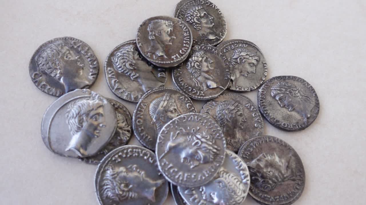 Antiguas monedas romanas de plata cayendo sobre un fondo neutro.