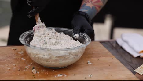 a man mixes chopped smoked fish with ingredients at bbq -smoker on cutting board cleans spatula with fingers concept: bbq, smoker, outside grilling, food preparation cookout