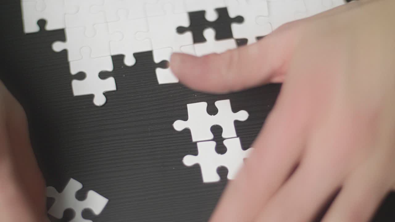 어두운 탁자 위에 놓여 있는 흰색 빈 퍼즐 조각을 닫고 젊은 남성의 손이 조각을 잡고 그것을 풀려고 합니다