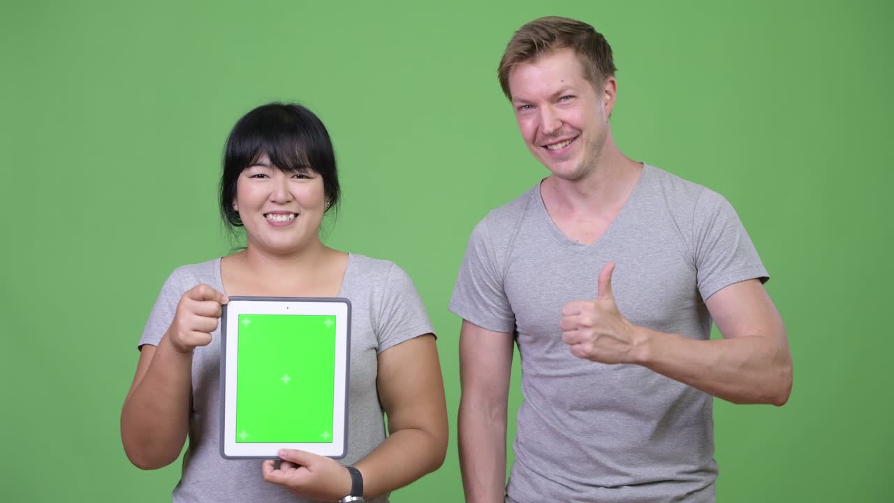Young happy multi-ethnic couple showing digital tablet and giving thumbs up together