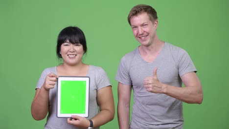 young happy multi-ethnic couple showing digital tablet and giving thumbs up together