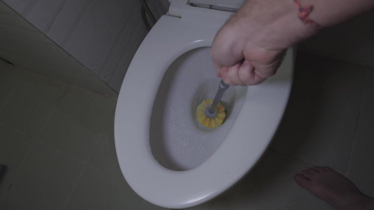 POV of a male vigorously scrubbing the inside of a white toilet bowl with a bristled cleaning brush