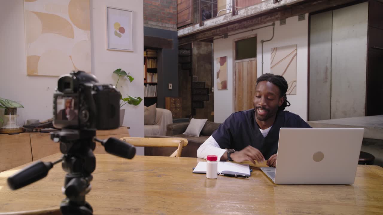 Pria Afrika-Amerika berseragam medis merekam dengan kamera DSLR di meja loteng, memeriksa catatan sambil menjelaskan label pil