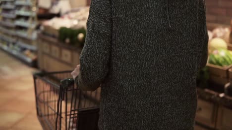 rare view of a woman is driving shopping trolley through food department in supermarket and looking around, picking bag with potatos