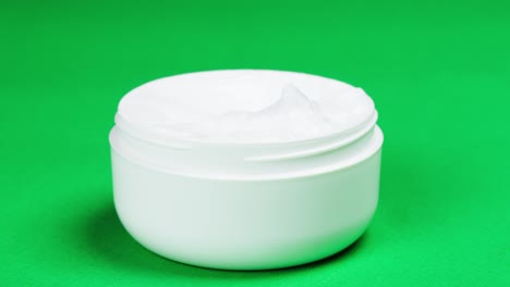 female hand taking moisturizing cream for face or body on green background. bowl with soft cream close-up, cosmetic texture. beauty and health, skin care concept