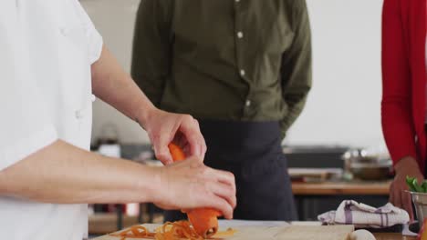 cocinera caucásica que enseña a un grupo diverso usando máscaras faciales