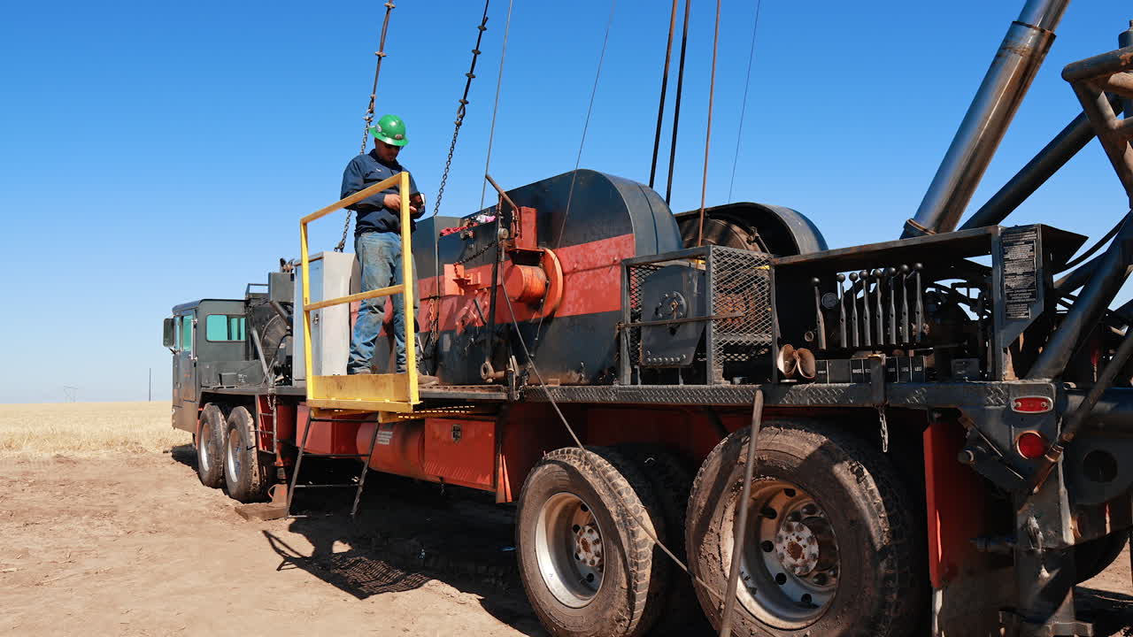 Worker stands at the deck of a huge truck with tower for oil/gas drilling. Equipment for boring natural resources.