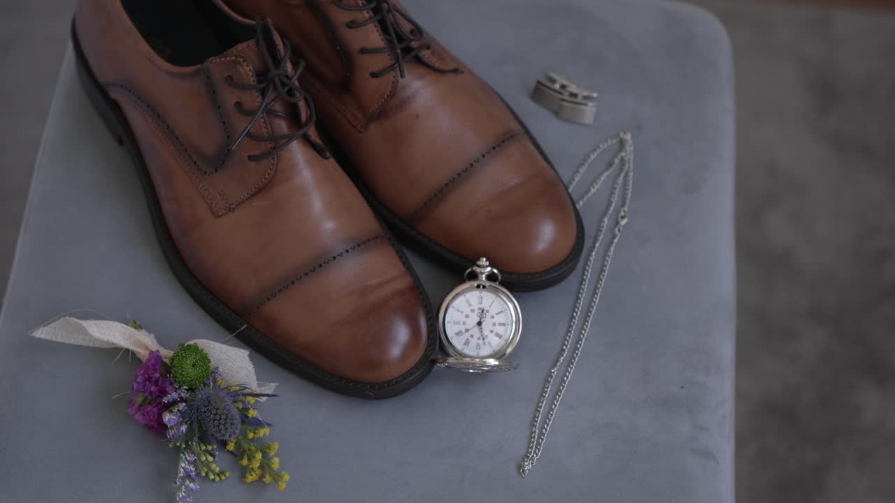 Brown leather dress shoes with a pocket watch, boutonniere, and cufflinks on fabric