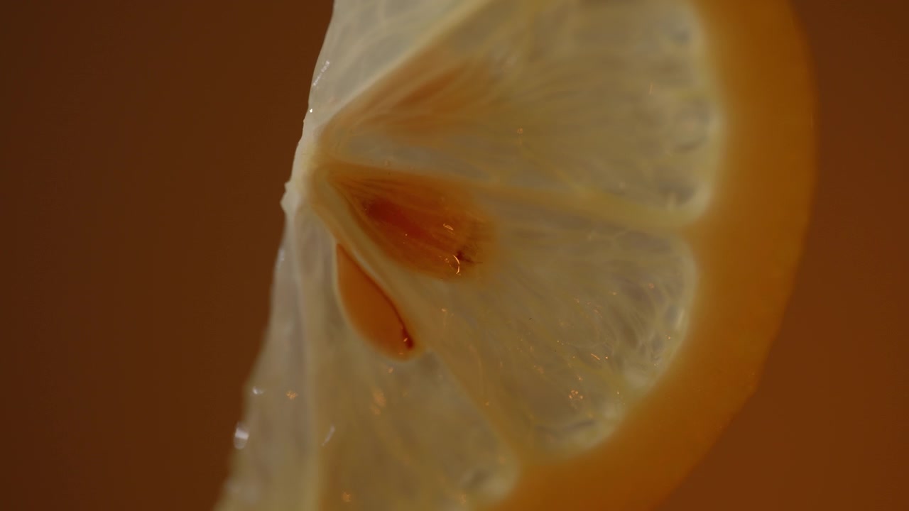 Fetta di limone calda retroilluminata che risplende con agrumi traslucidi e semi, sfondo con sfumatura arancione, dettaglio macro