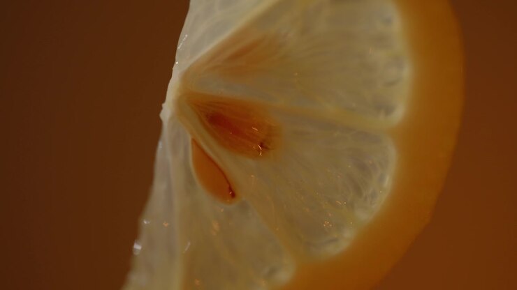 Fetta di limone calda retroilluminata che risplende con agrumi traslucidi e semi, sfondo con sfumatura arancione, dettaglio macro