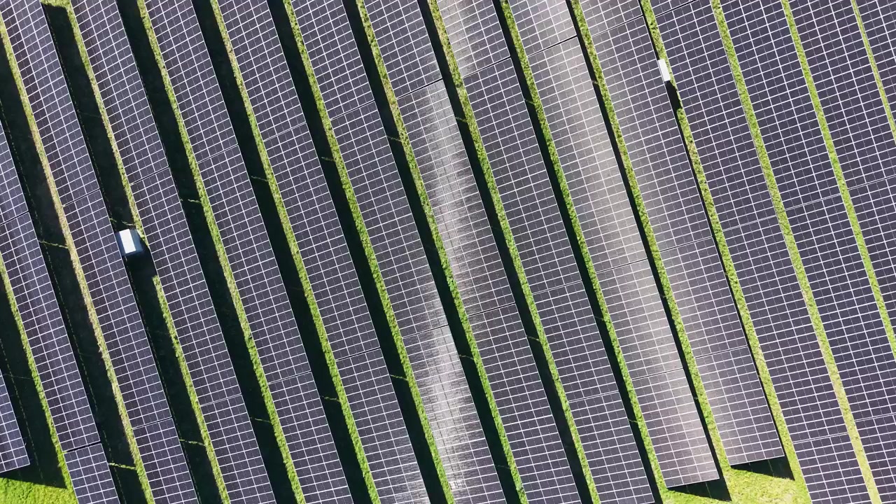 Una ripresa aerea con drone dall'alto che sorvola una centrale solare adiacente a un campo di colza giallo in fiore nella Danimarca rurale
