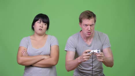 hombre joven jugando juegos mientras la mujer asiática con sobrepeso parece molesta