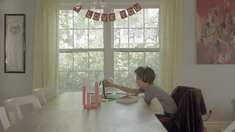 wide of teen boy at a dining room table of a nice home at a tablet in virtual learning