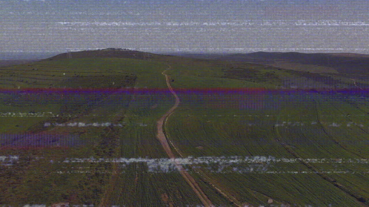 Distorsione che causa linee statiche in una vista aerea di una strada sterrata che attraversa campi, mostrando terreni agricoli.