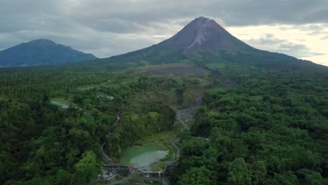 Vuelo-Aéreo-Hacia-Atrás-Que-Muestra-Un-Lago-Natural-Rodeado-Por-El-Desierto-De-Indonesia-Y-El-Volcán-Merapi-Gigante-En-El-Fondo-Durante-El-Verano---Bego-Pendem,-Indonesia