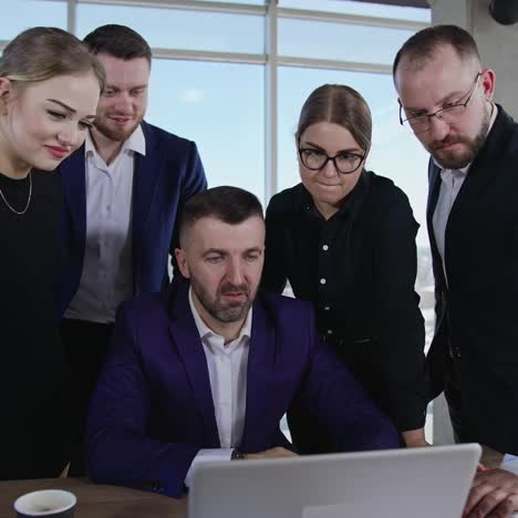teammates stand around the table and laptop. team of males and females discuss something on computer screen. friendly communication of coworkers in the office