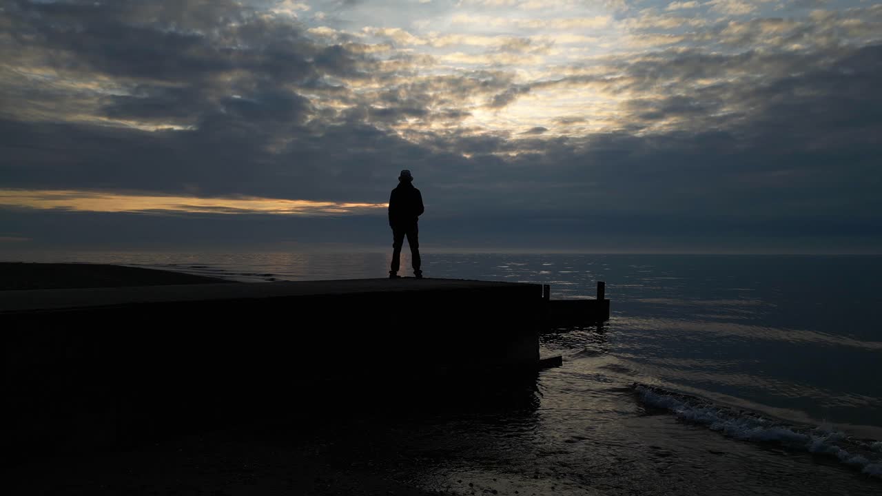 silueta de un hombre en cámara lenta al final del muelle mirando hacia el mar al atardecer en la playa de fleetwood, lancashire, reino unido