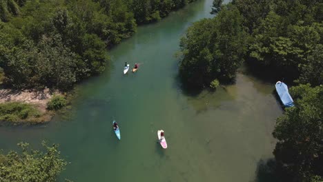 Vista-Aérea-De-Aves-Ahogadas-Moviéndose-Lentamente-Hacia-Atrás-Dolly-De-Paddle-Boarders-Remando-Lentamente-Río-Arriba-Rodeado-De-Jungla-Tropical