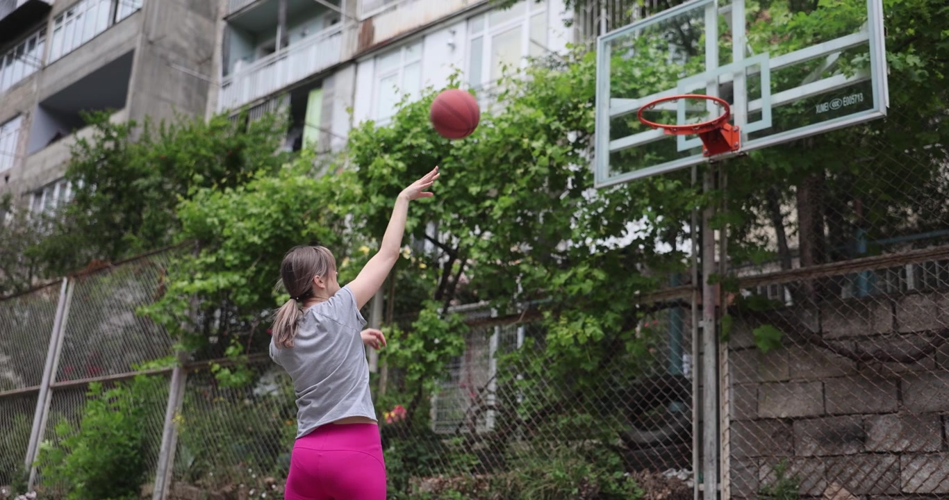 Young woman athlete plays basketball shooting hoops on court