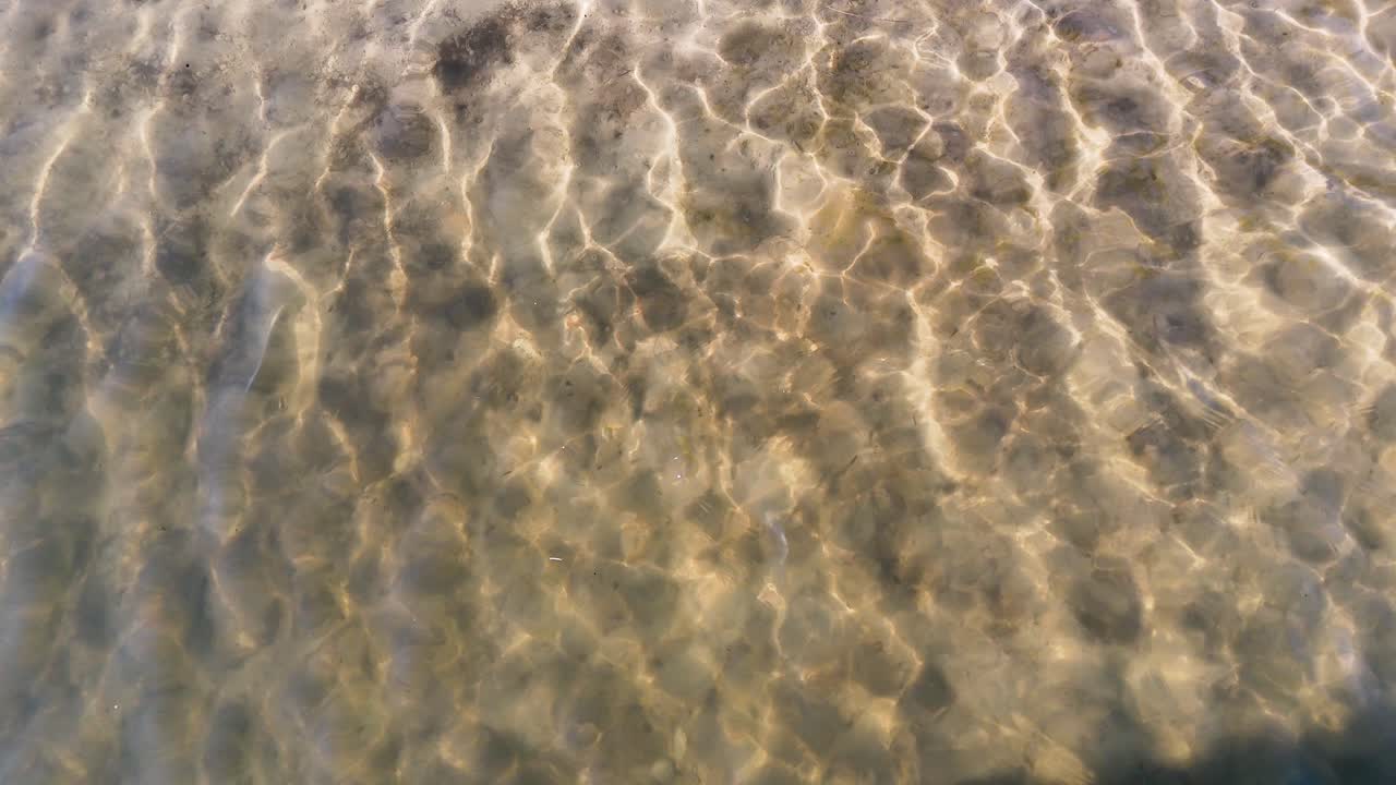 Rippling sunlight reflections dance across shallow, clear water with tranquil, natural textures and patterns