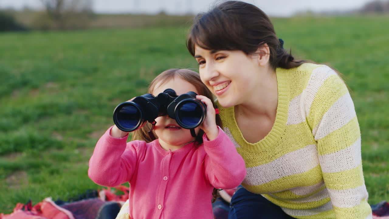 A Young Mother Shows Her Hand To The Distance And Her Little Daughter Looks Carefully Through Binocu