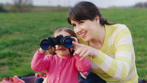 a young mother shows her hand to the distance and her little daughter looks carefully through binocu