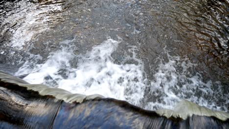 Closeup overlooking small flowing copper woodland river cascading into waterfall