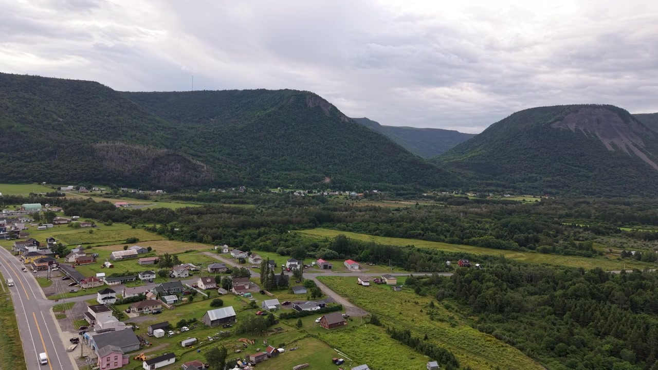 Ampia vista aerea di un villaggio costiero circondato da montagne verdi e una valle a Mont Saint-Pierre, Gaspésie, Quebec, Canada, riprese con drone