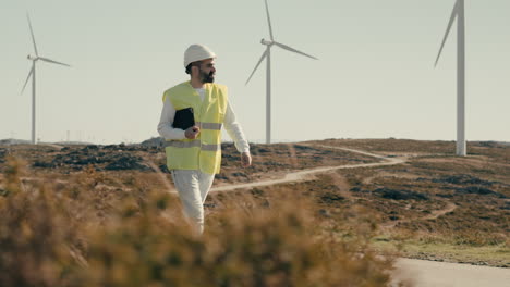 a male caucasian renewable energy expert in safety gear inspects wind turbines while walking, symbolizing our commitment to clean energy