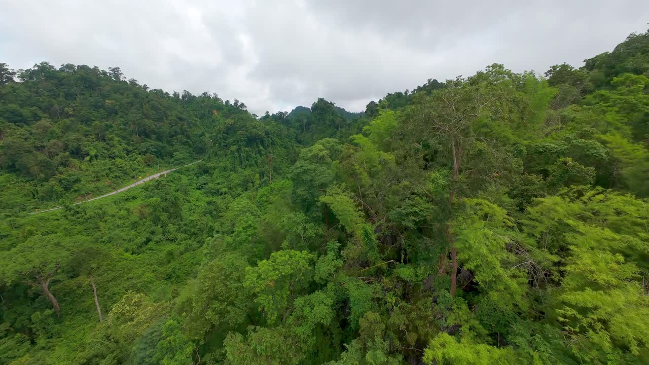 Aerial drone shot ascending above dense jungle and mountains with clouds and mist in the distance near Sangkhla in Thailand
