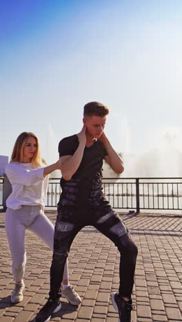 street dance. young couple of professional dancers on the background of beautiful fountain outdoors. boy in black and girl in white performing freestyle dance. vertical video