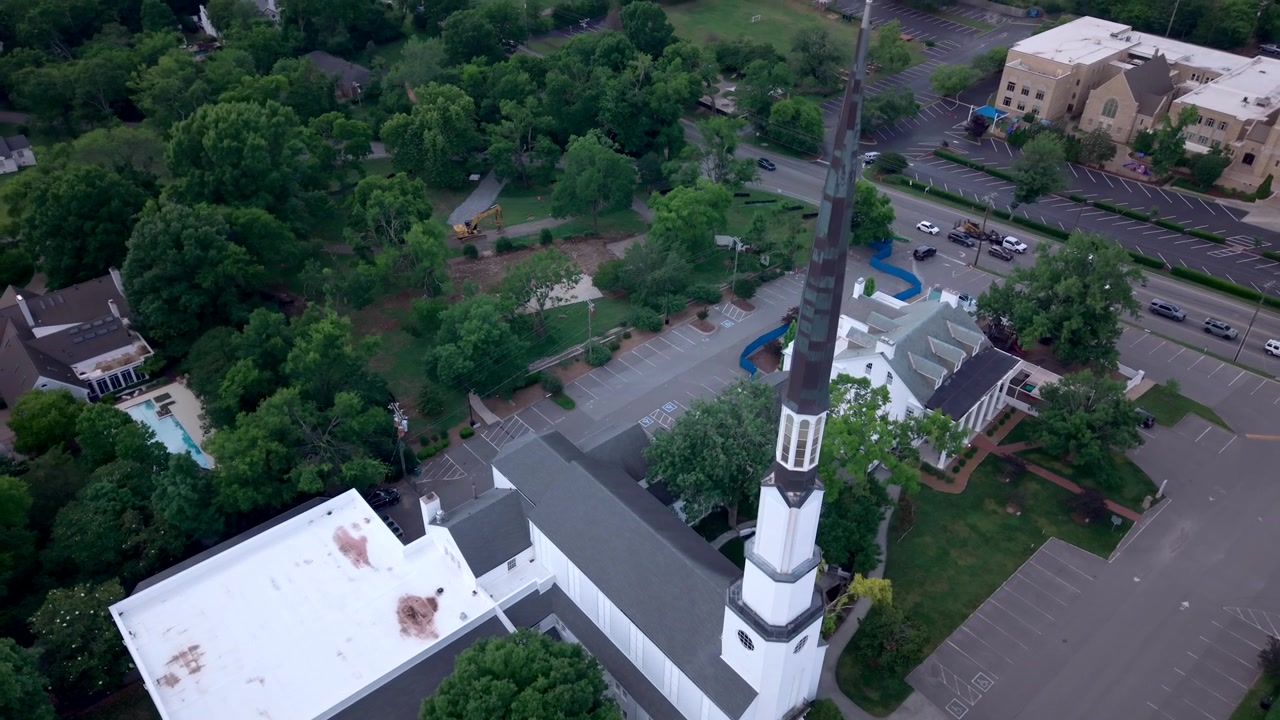 Igreja Cristã e Pré-escola Woodmont em Nashville, revelando sua torre, pináculo e casas circundantes, em tomada aérea ascendente.