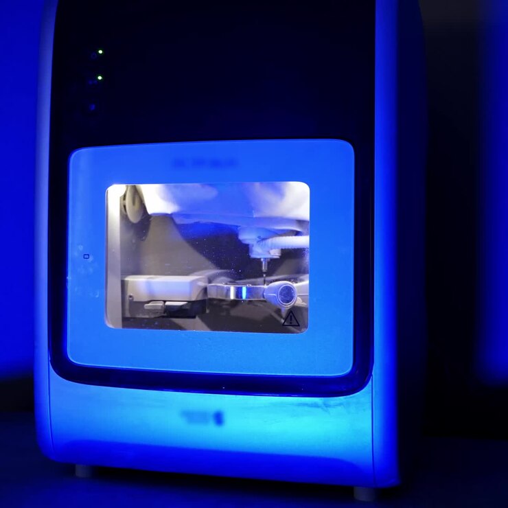 Tecnologia avanzata in odontoiatria. Lavori della fresatrice dentale che scolpiscono la forma dei denti umani in luce blu.