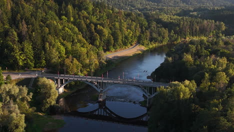 landmark bridge in sigulda, latvia. aerial view of cars traveling across the concrete bridge over the gauja river surrounded by lush green vegetation.