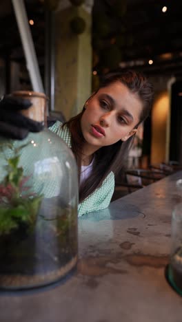 mujer manejando cuidadosamente plantas de terrario en un café