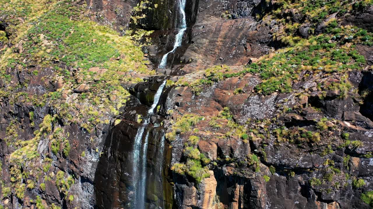 Aerial view tracking up steep, cascading waterfall with double rainbow