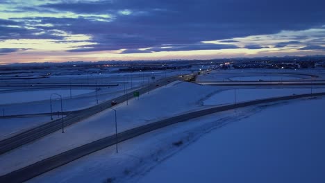 vehicles on snowy highway overpass at dusk, aerial