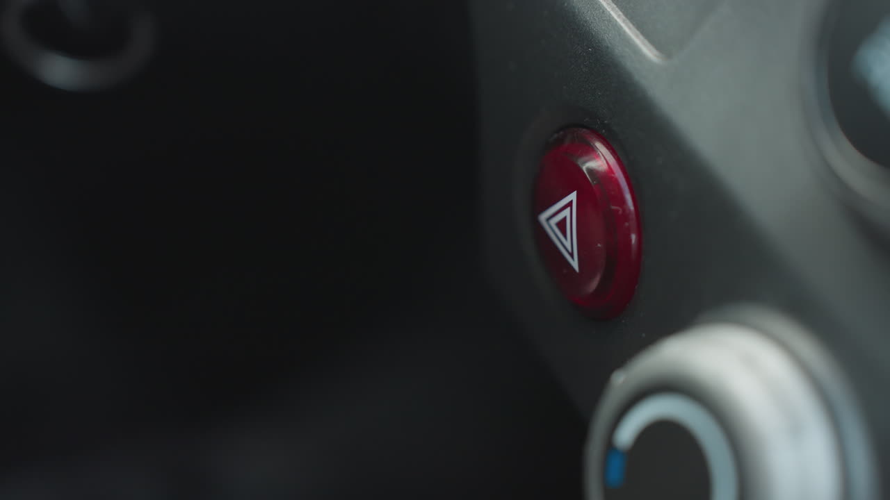 Top down view of fair skinned person pressing hazard button on car dashboard console near climate control dial showing finger interaction with red emergency switch under ambient light
