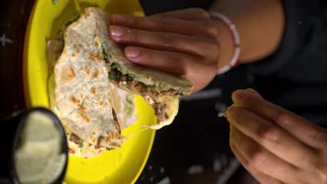 movimiento lento vertical de un par de manos de una mujer sosteniendo un taco de quesadilla en un plato amarillo y exprimir un poco de jugo de limón de lima en