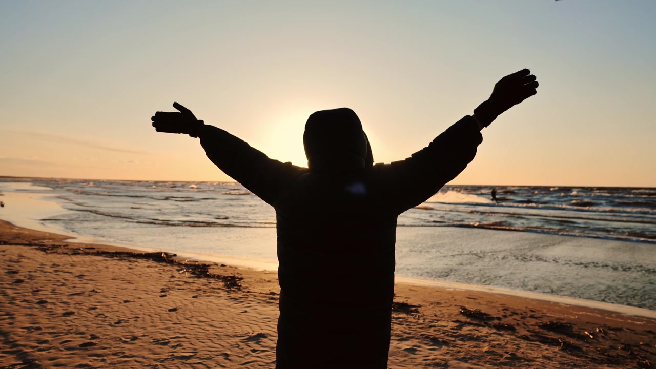 Une femme ouvre les bras vers un coucher de soleil éclatant tandis que des cerfs-volants lointains traversent l'horizon marin