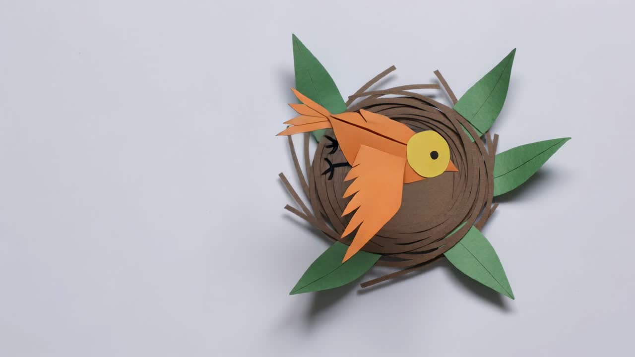 Stop-motion-billeder skrider frem, hvor en orange papirfugl går ind i en rede på et hvidt bord og gemmer sig under blade.