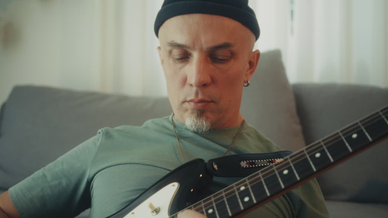 Primo piano di un uomo che suona la chitarra elettrica sul divano di casa.