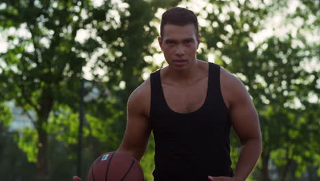 focused muscular streetball male player practicing basketball alone outdoor.